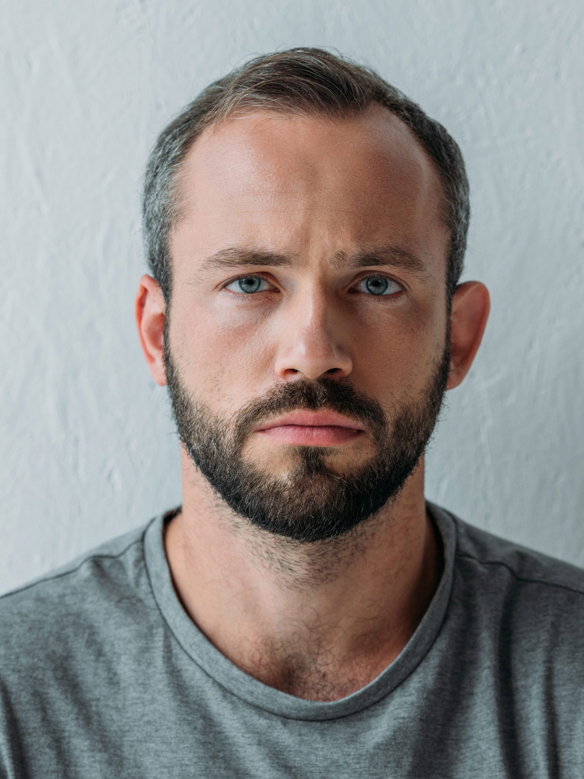 portrait of unhappy bearded man looking at camera on grey