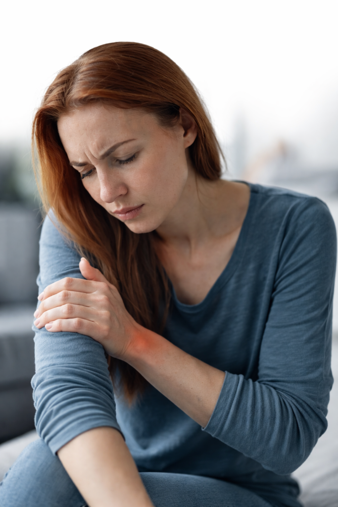 Woman holding her wrist and forearm, looking down with a distressed expression.